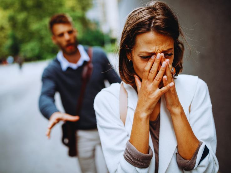 Donna in lacrime inseguita da uomo con espressione rabbiosa