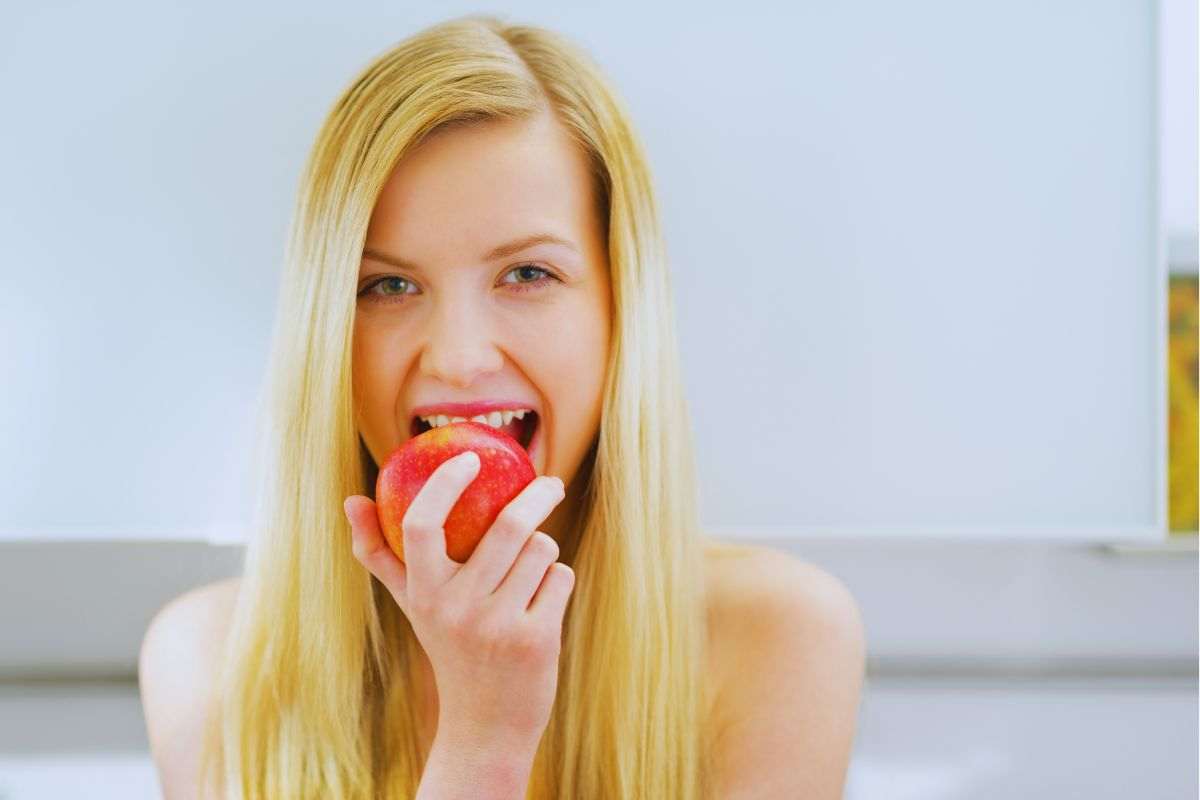 Ragazza che addenta una mela rossa