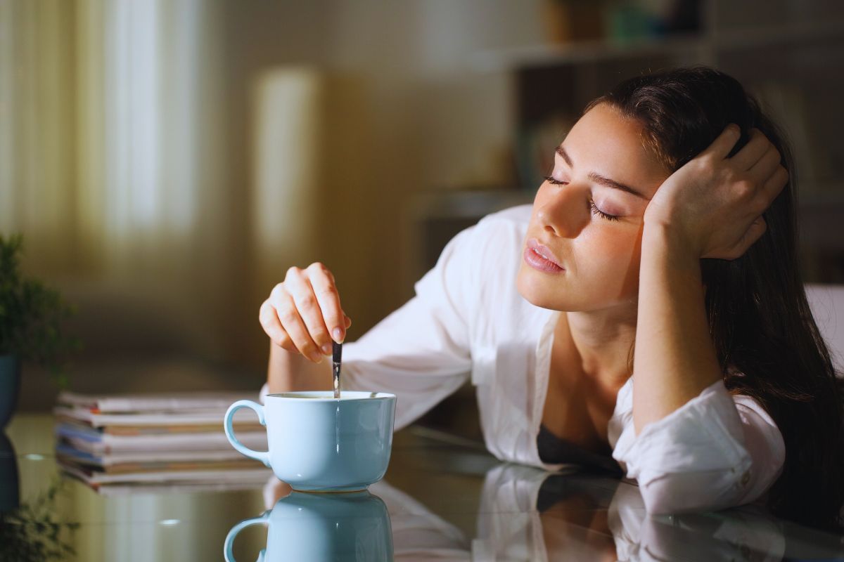 Donna appena sveglia che mescola lo zucchero nel caffè