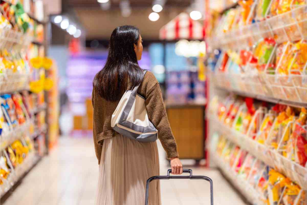 donna al supermercato con cestino tra le corsie